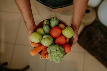 A person is holding bowl full of colorful vegetables, including broccoli, carrots, and apples.