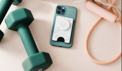 There is a set of green dumbells, a resistant band, a water bottle and a cell phone all laid out on a yoga mat