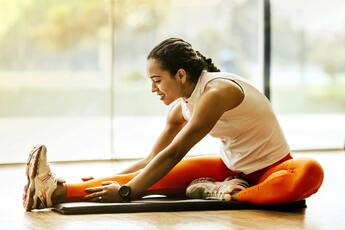 A woman in a gray top and black pants is doing a side stretch. 
