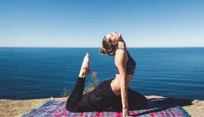 A woman in black leggings and top is doing a yoga pose on the beach 
